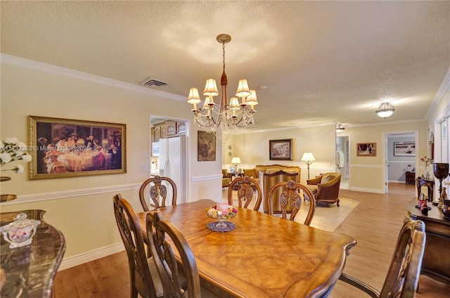 dining space featuring an inviting chandelier, crown molding, a textured ceiling, and light wood-type flooring