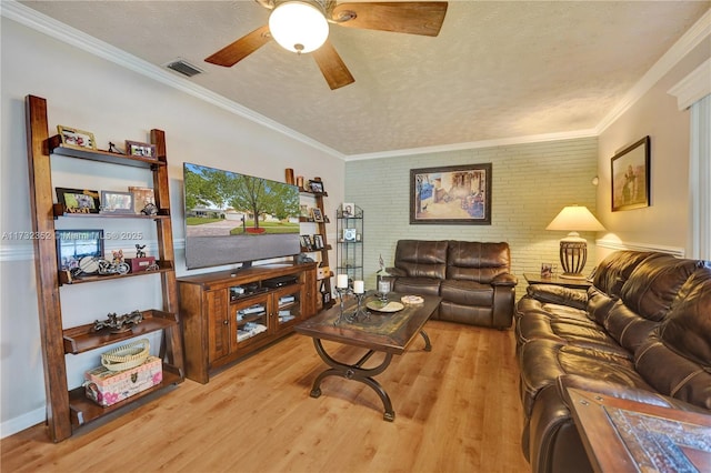 living room with ceiling fan, ornamental molding, a textured ceiling, brick wall, and light wood-type flooring