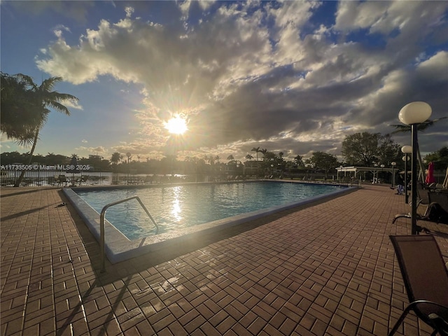 pool at dusk with a patio and a water view