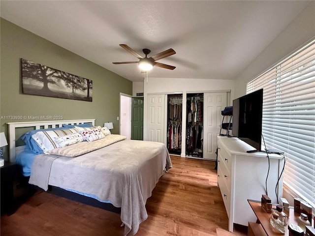 bedroom with multiple closets, light hardwood / wood-style floors, and ceiling fan