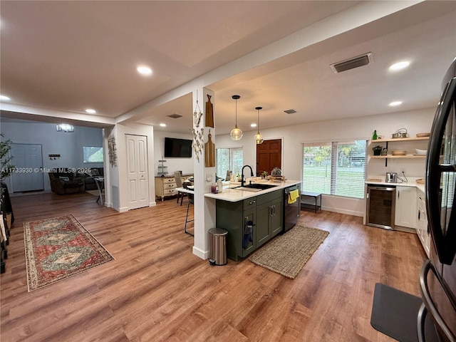 kitchen featuring sink, a kitchen island with sink, black appliances, decorative light fixtures, and beverage cooler