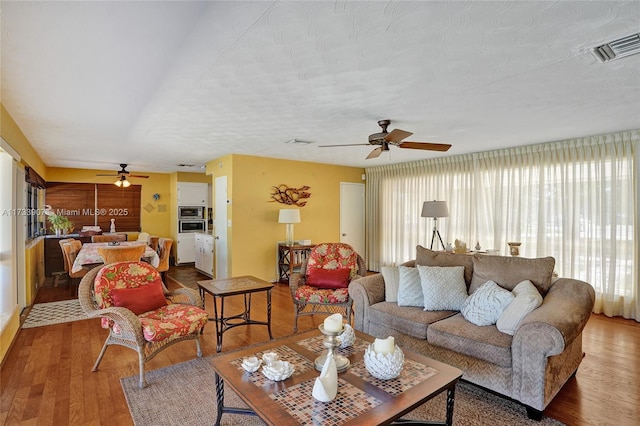 living room featuring hardwood / wood-style flooring, ceiling fan, and a textured ceiling