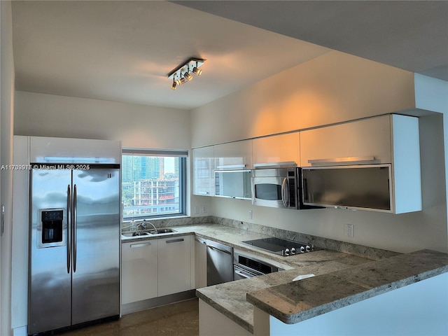 kitchen featuring a sink, a peninsula, light stone counters, white cabinetry, and appliances with stainless steel finishes