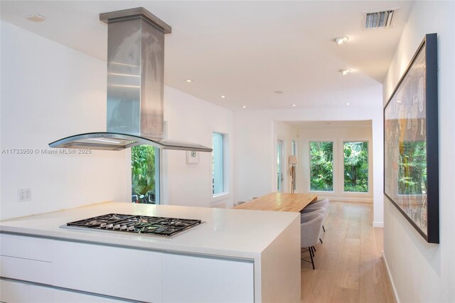 kitchen featuring white cabinetry, light hardwood / wood-style floors, stainless steel gas stovetop, and island exhaust hood