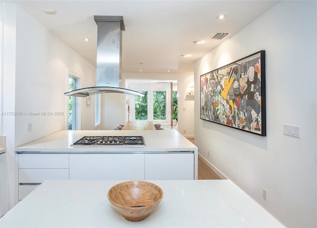 kitchen with kitchen peninsula, island exhaust hood, stainless steel gas stovetop, hardwood / wood-style floors, and white cabinets