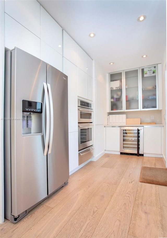 kitchen featuring appliances with stainless steel finishes, beverage cooler, light hardwood / wood-style flooring, and white cabinets