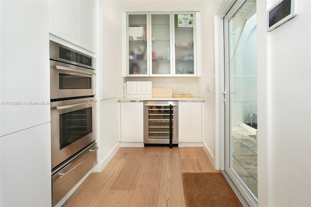 kitchen featuring white cabinetry, stainless steel double oven, beverage cooler, and light hardwood / wood-style floors