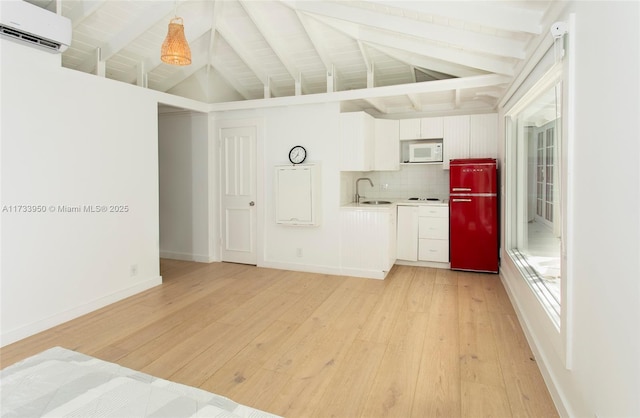 kitchen with a wall mounted air conditioner, decorative light fixtures, white cabinetry, fridge, and light hardwood / wood-style floors