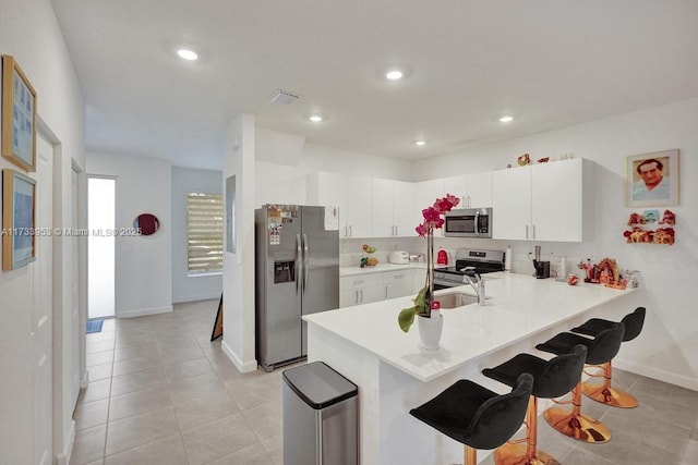 kitchen with sink, a breakfast bar area, appliances with stainless steel finishes, white cabinetry, and kitchen peninsula