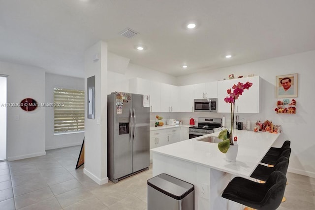 kitchen with a breakfast bar, white cabinetry, light tile patterned floors, kitchen peninsula, and stainless steel appliances