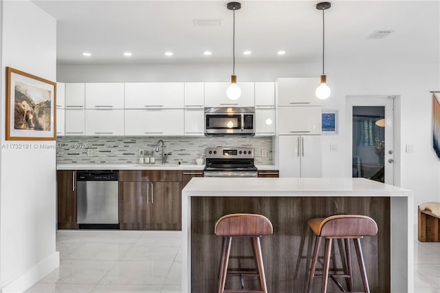 kitchen with appliances with stainless steel finishes, sink, white cabinets, and decorative light fixtures