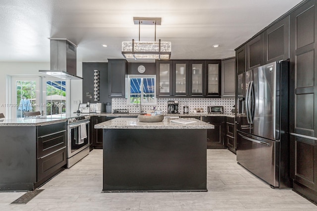 kitchen with light stone counters, island range hood, appliances with stainless steel finishes, a kitchen island, and pendant lighting