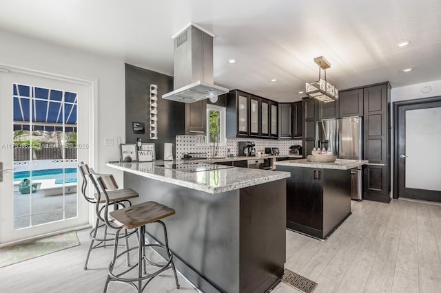 kitchen featuring dark brown cabinetry, decorative light fixtures, kitchen peninsula, island exhaust hood, and black electric stovetop