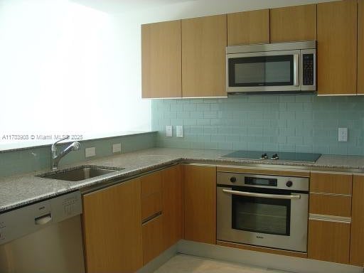 kitchen featuring light stone counters, appliances with stainless steel finishes, sink, and backsplash