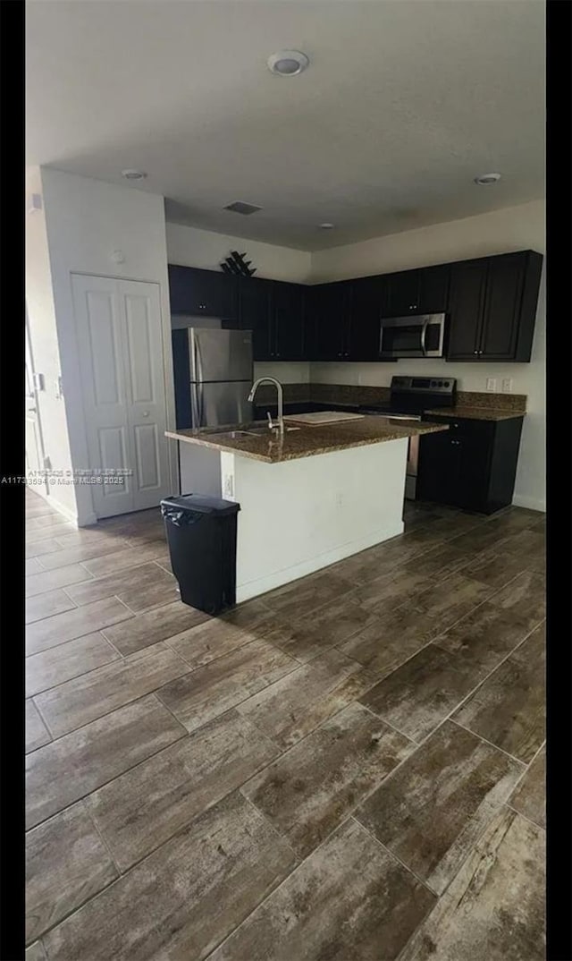 kitchen with stainless steel appliances, a kitchen island with sink, dark wood-type flooring, and a breakfast bar