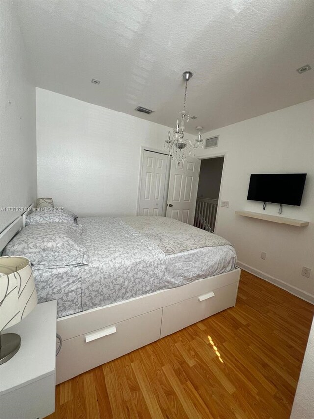 bedroom with an inviting chandelier, wood-type flooring, and a textured ceiling