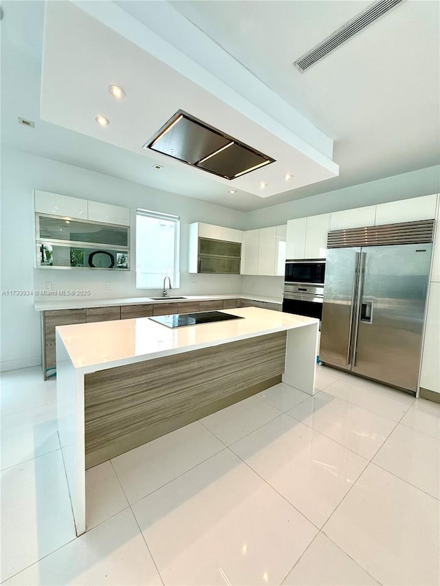 kitchen with sink, black appliances, light tile patterned floors, a large island, and white cabinets