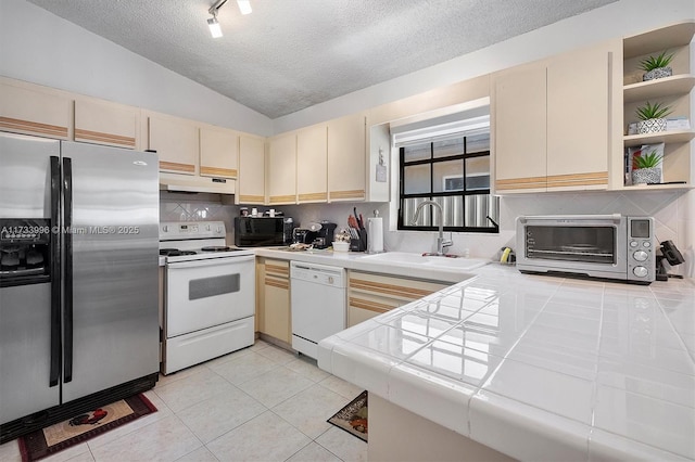 kitchen with lofted ceiling, sink, tile counters, white appliances, and cream cabinetry