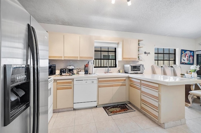 kitchen featuring stainless steel fridge with ice dispenser, dishwasher, sink, kitchen peninsula, and cream cabinetry