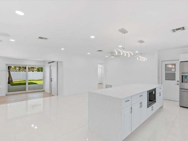 kitchen with a kitchen island, appliances with stainless steel finishes, decorative light fixtures, white cabinets, and wall chimney exhaust hood