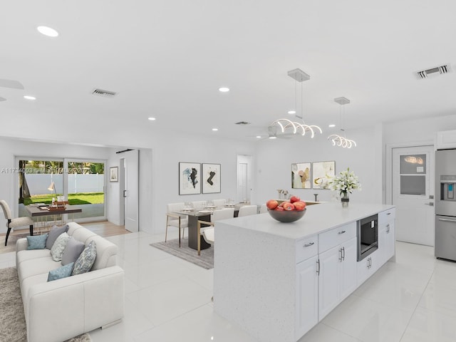 kitchen with built in microwave, white cabinetry, decorative light fixtures, a center island, and stainless steel fridge