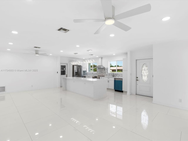 kitchen featuring white cabinetry, a center island, pendant lighting, stainless steel appliances, and wall chimney range hood