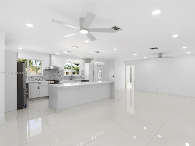 kitchen featuring pendant lighting, white cabinets, stainless steel fridge, a large island, and wall chimney range hood