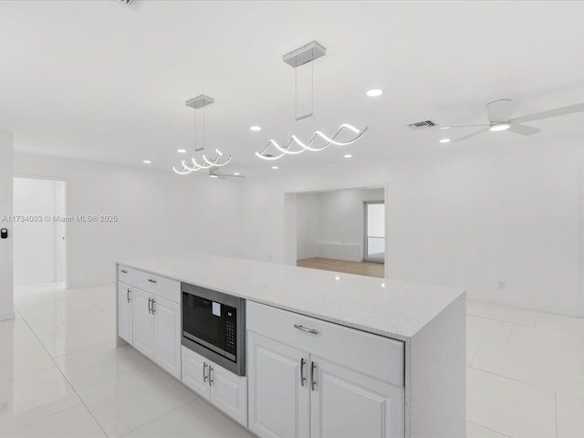 kitchen featuring built in microwave, light tile patterned flooring, light stone counters, pendant lighting, and white cabinets