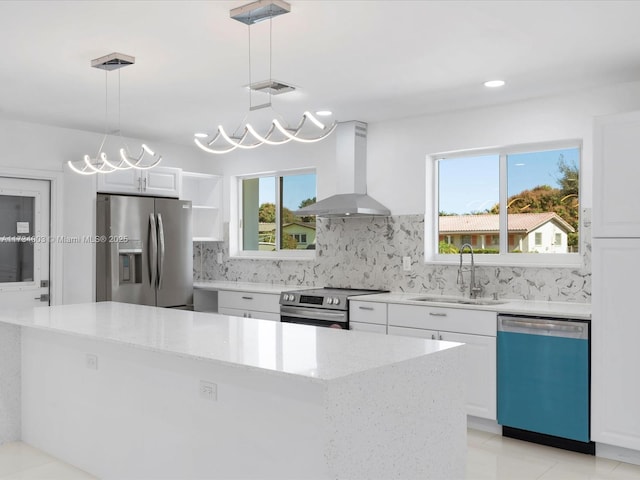 kitchen with appliances with stainless steel finishes, island range hood, white cabinets, and decorative light fixtures