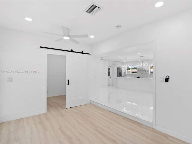 spare room featuring ceiling fan, a barn door, and light wood-type flooring