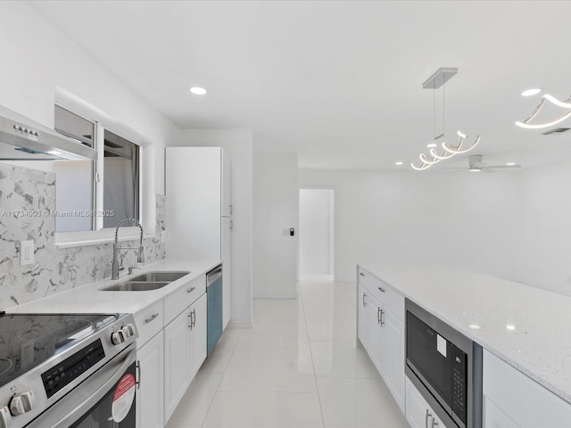 kitchen featuring sink, stainless steel appliances, light stone counters, white cabinets, and decorative light fixtures