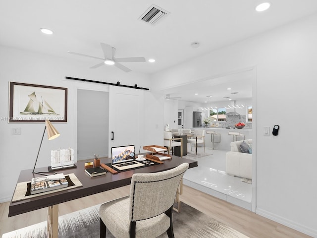 office space with wood-type flooring, a barn door, and ceiling fan