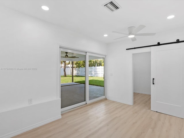 spare room with ceiling fan, a barn door, and light hardwood / wood-style flooring