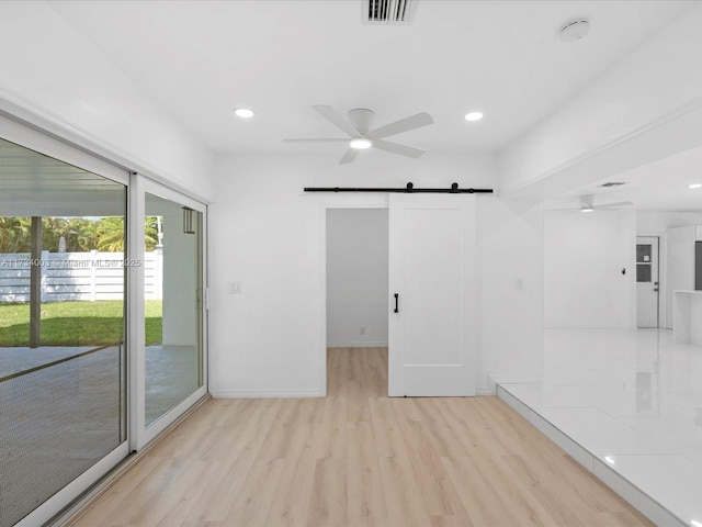 empty room with light hardwood / wood-style floors, a barn door, and ceiling fan