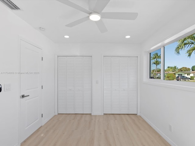 unfurnished bedroom featuring ceiling fan, light hardwood / wood-style flooring, and multiple closets