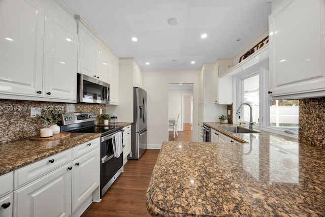 kitchen with appliances with stainless steel finishes, sink, dark stone counters, and white cabinets