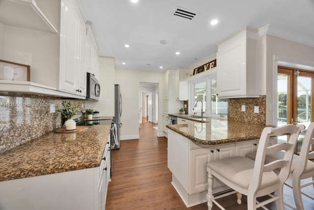 kitchen with dark stone countertops, a kitchen breakfast bar, stainless steel appliances, white cabinets, and kitchen peninsula