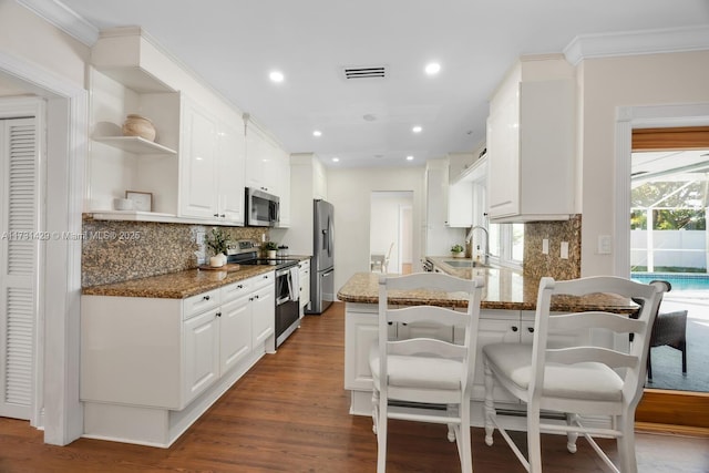 kitchen featuring stainless steel appliances, dark hardwood / wood-style floors, kitchen peninsula, white cabinets, and dark stone counters