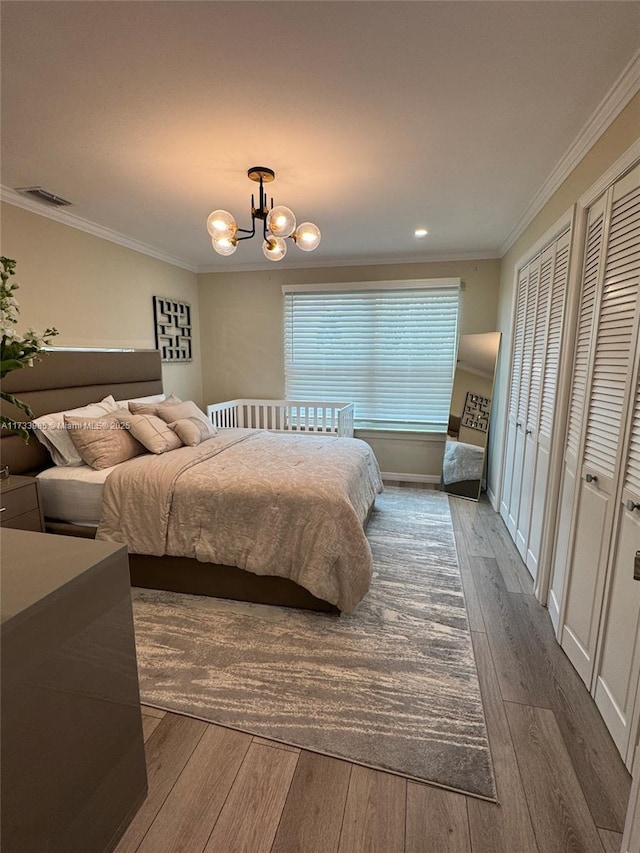 bedroom with a notable chandelier, crown molding, dark wood-type flooring, and two closets