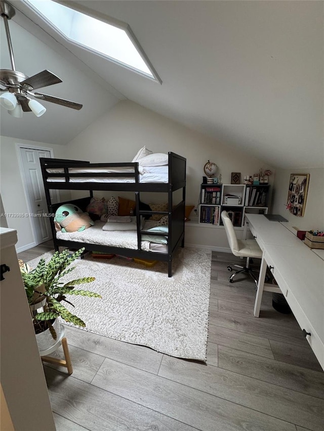 bedroom with ceiling fan, vaulted ceiling with skylight, and hardwood / wood-style floors