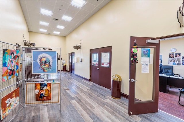 corridor featuring a towering ceiling, hardwood / wood-style floors, and a drop ceiling