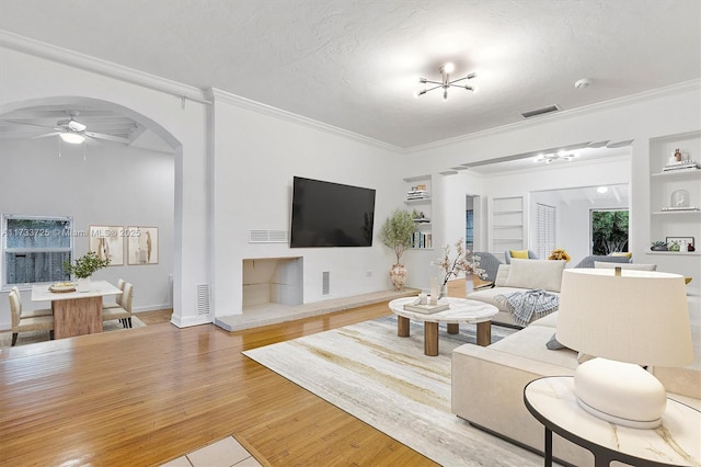 living room with a textured ceiling, built in shelves, arched walkways, and wood finished floors