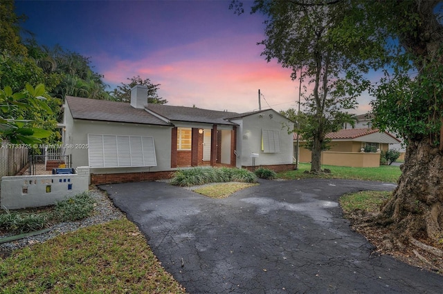 view of front of property featuring brick siding, fence, driveway, and stucco siding