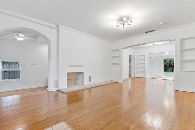 unfurnished living room with built in features, arched walkways, visible vents, and light wood-style flooring