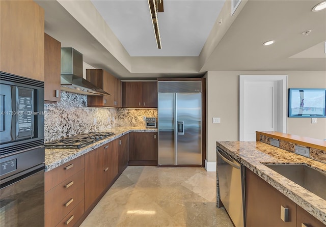 kitchen featuring wall chimney range hood, sink, tasteful backsplash, black appliances, and light stone countertops