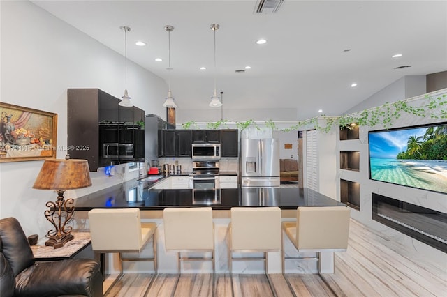 kitchen featuring vaulted ceiling, pendant lighting, a breakfast bar area, kitchen peninsula, and stainless steel appliances