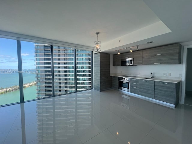 kitchen with light tile patterned flooring, pendant lighting, a wall of windows, stainless steel appliances, and a water view