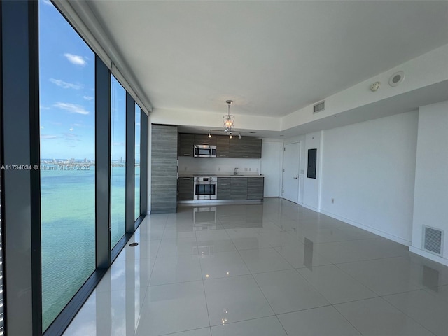 unfurnished living room featuring light tile patterned floors, electric panel, expansive windows, and a water view