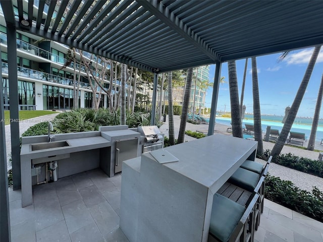 view of patio with area for grilling, sink, a pergola, and a water view