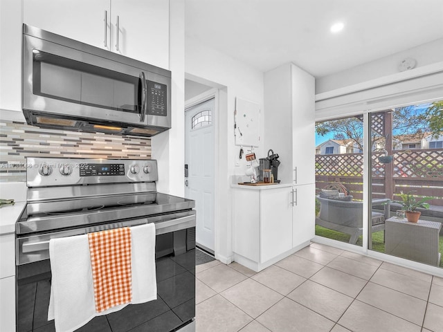 kitchen featuring stainless steel appliances, light tile patterned flooring, white cabinets, and decorative backsplash